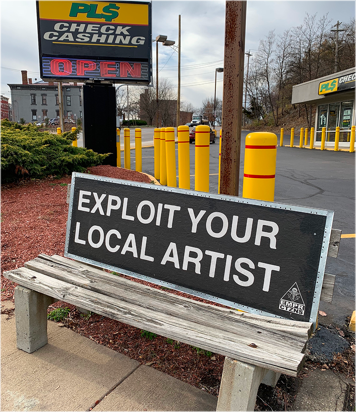 Bench sign reading "Exploit Your Local Artist.